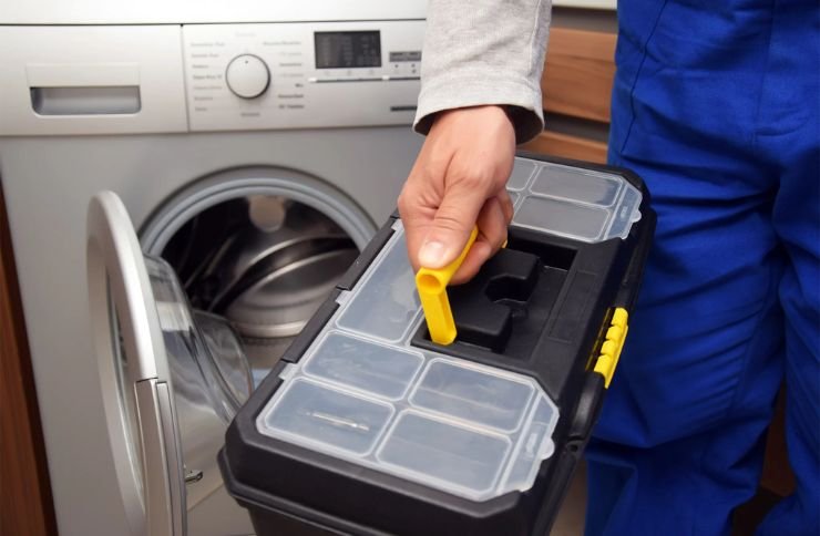 A man is positioned next to a washing machine, holding a toolbox for laundry appliance repair services in Renton, WA.