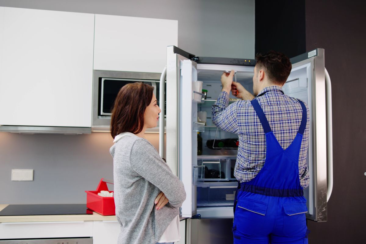 A couple stands in front of a refrigerator, examining it for specific problems that may need attention.