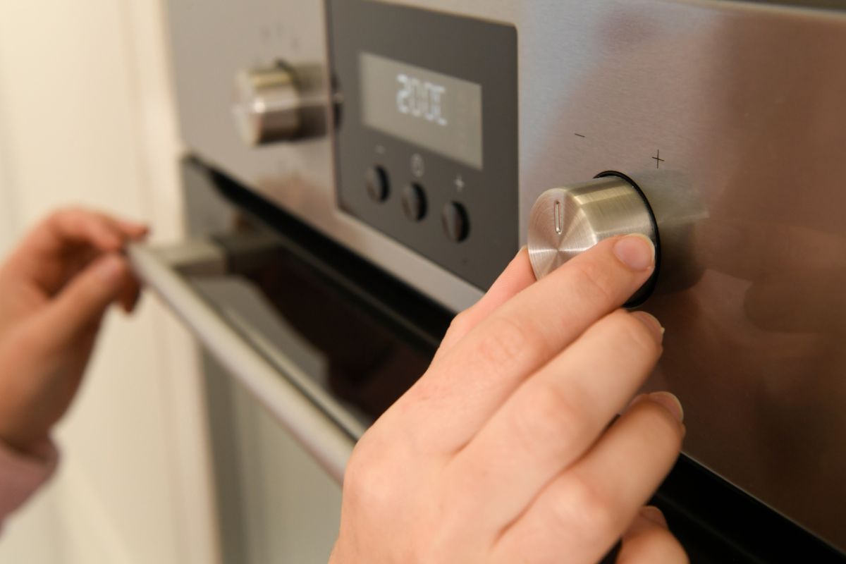  An individual is turning the oven knob, ensuring the correct temperature is set for their culinary preparations.