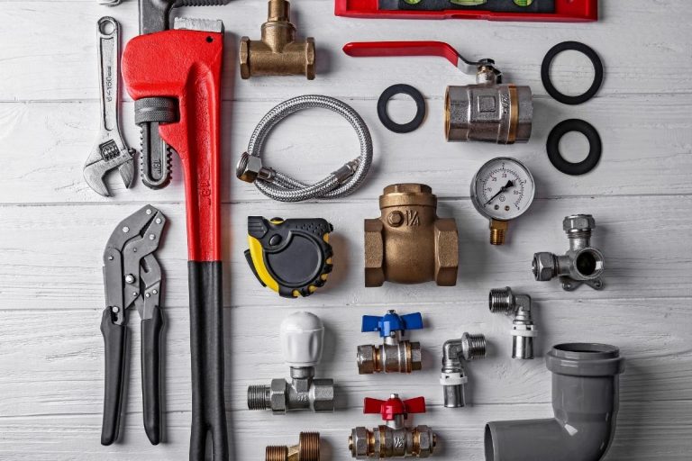 Various plumbing tools and accessories displayed on a white table, showcasing wrenches, pipes, and fittings.